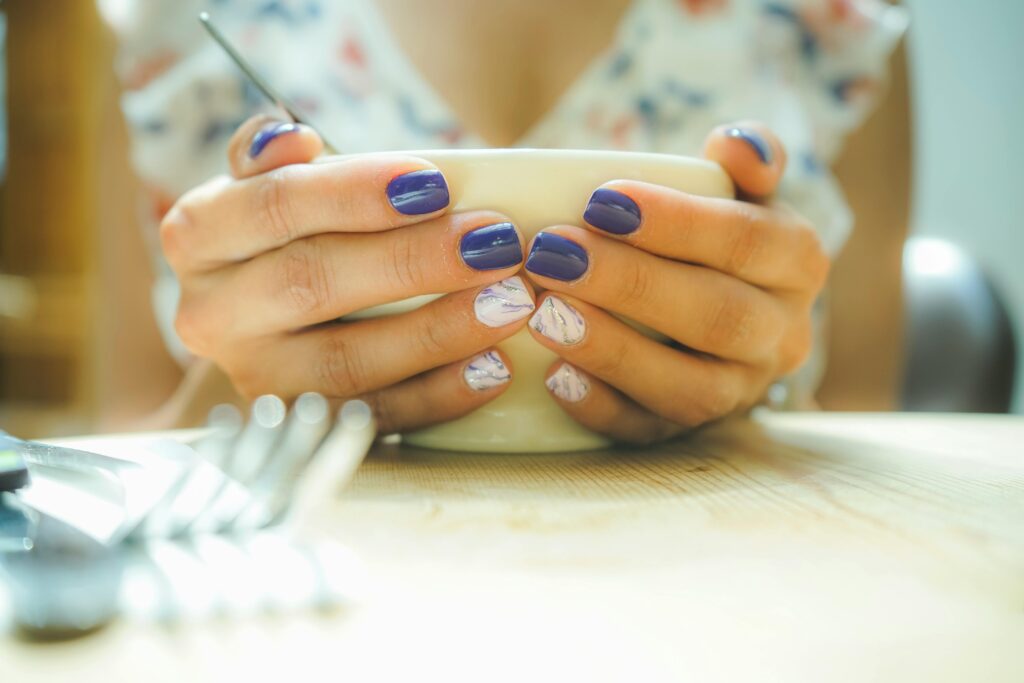 A woman with colorful nails holds a mug, capturing a moment of warmth and style indoors.